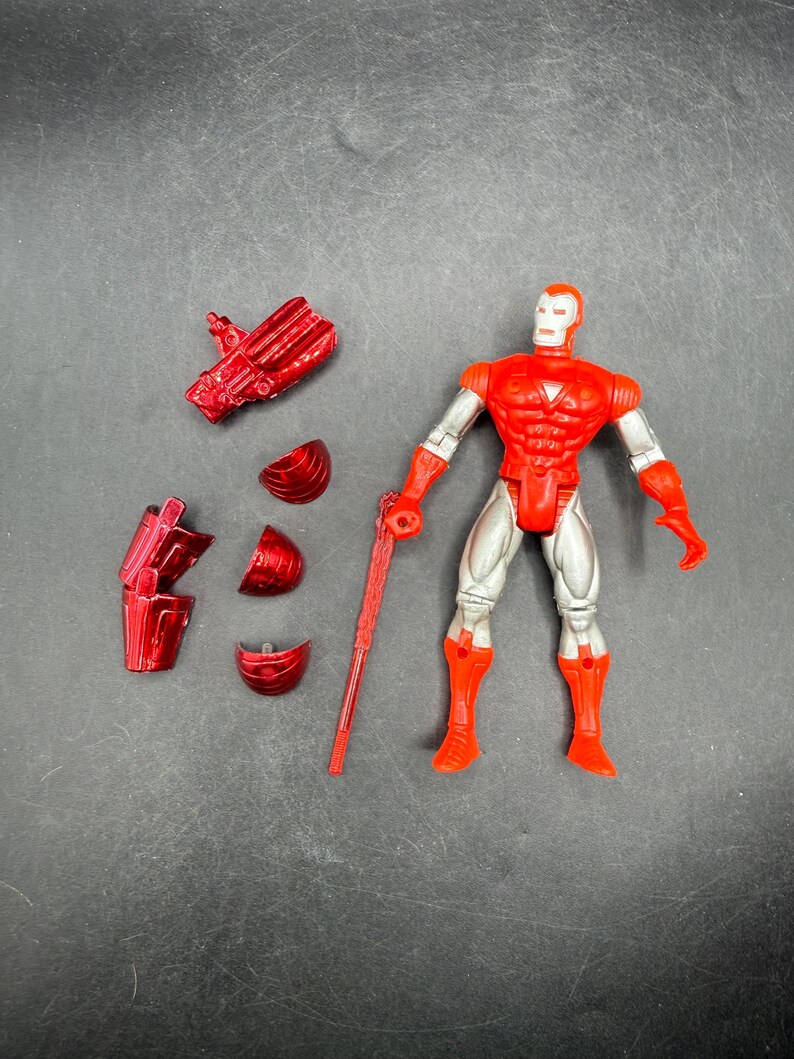 Puede incluir: Una figura de acci&oacute;n roja y plateada de un superh&eacute;roe con piezas de armadura desmontables y un bast&oacute;n rojo. La figura tiene un torso, brazos y piernas rojos, con detalles plateados. La figura est&aacute; de pie.