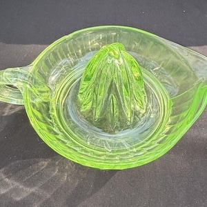 Puede incluir: Exprimidor de cítricos vintage de vidrio verde claro. El exprimidor tiene un reamer acanalado en el centro, una boquilla y un asa. El vidrio tiene un diseño texturizado y acanalado. Diseñado para extraer jugo de cítricos.