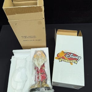以下が含まれることがあります： Disney Auctionsのグランピーのボブルヘッドフィギュア。透明なプラスチックと白い発泡スチロールで梱包されています。「DISNEY AUCTION ITEM # A06420 / BOBBLE HEAD-GRUMPY」と書かれた無地の段ボール箱と、Disney Auctionsのロゴが入った白い箱がセットになっています。