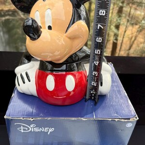 May include: A Mickey Mouse figurine, black ears, tan face, and red shorts. The figurine is on a blue box with the Disney logo and the word "HARDWARE". The figurine measures approximately 6 inches in height.