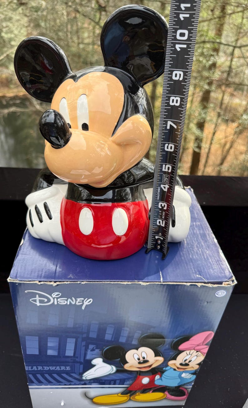 May include: A Mickey Mouse figurine, black ears, tan face, and red shorts. The figurine is on a blue box with the Disney logo and the word "HARDWARE". The figurine measures approximately 6 inches in height.