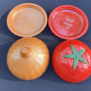 May include: A plastic onion-shaped food storage container in light brown and a tomato-shaped food storage container in red with a green stem. The tomato container base features text instructions for storing tomatoes with the cut side face down.