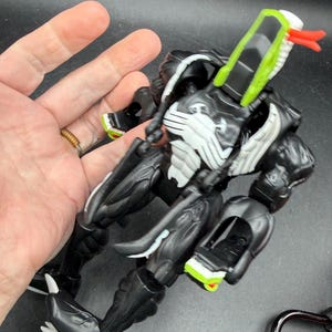 May include: Black and white action figure with green and red detailing. The figure has a snake-like head and a muscular build. A collectible toy.
