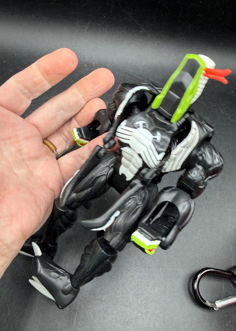 May include: Black and white action figure with green and red detailing. The figure has a snake-like head and a muscular build. A collectible toy.