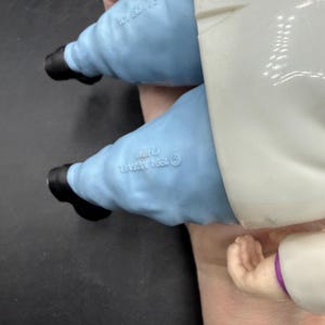 May include: A vintage action figure featuring light blue pants, black shoes, and a white coat. The figure is held by a hand. The figure is marked with "&copy; 1994 MARVEL" and "CHINA".