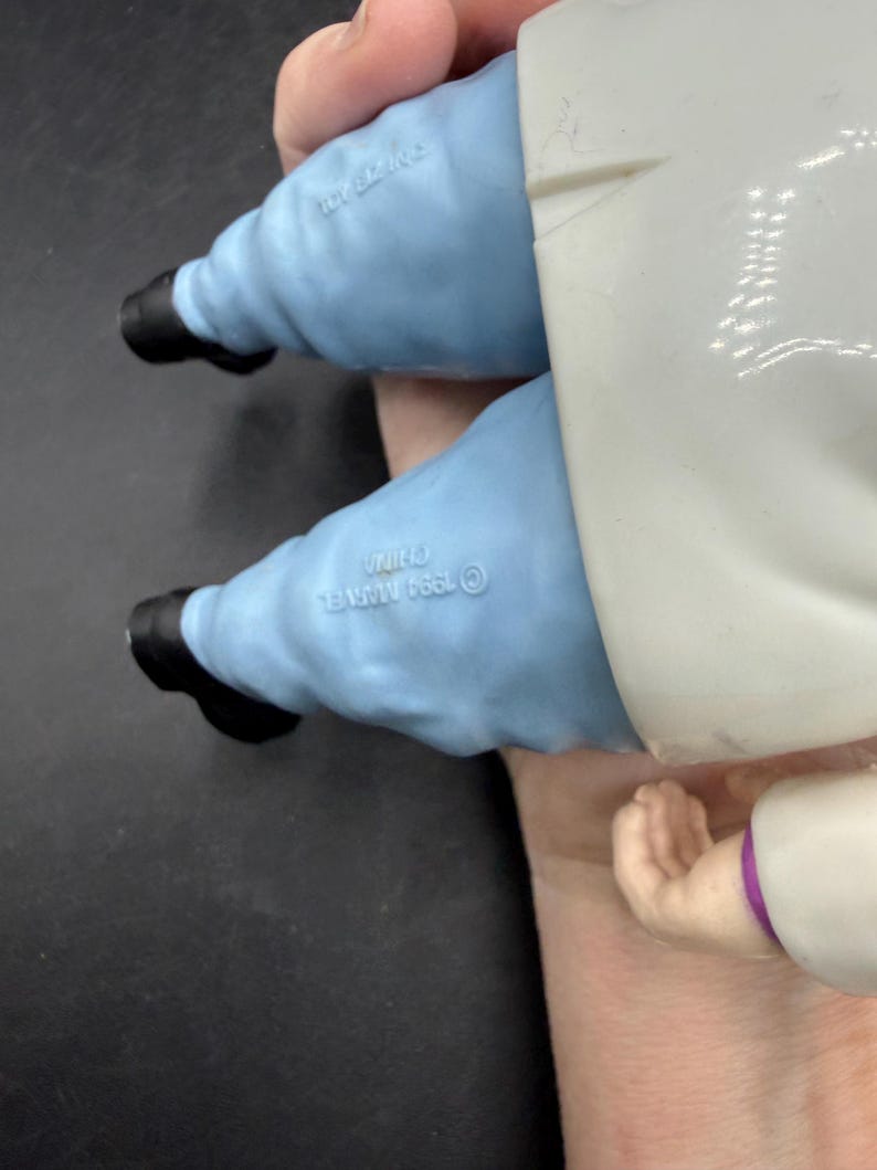 May include: A vintage action figure featuring light blue pants, black shoes, and a white coat. The figure is held by a hand. The figure is marked with "&copy; 1994 MARVEL" and "CHINA".