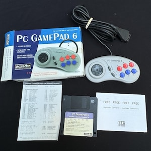 May include: A gray PC Gamepad 6 controller with red and blue buttons, a directional pad, and a black cable. The box and a 3.5-inch floppy disk are also visible. The box has the text "PC GAMEPAD 6" and "INTERNET".
