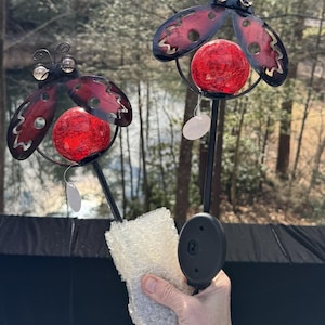 May include: Two red ladybug solar garden lights with clear glass globes. The lights are on black metal stakes and have a black solar panel on the back.