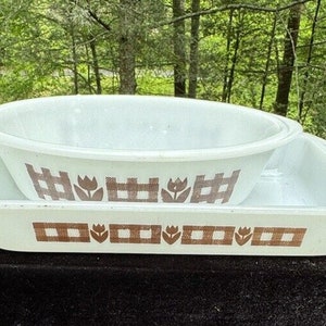 Puede incluir: Un plato para hornear de cerámica blanca con un diseño de tulipán marrón y blanco. El plato está anidado dentro de un plato para hornear de cerámica blanca más grande con un diseño a cuadros marrón y blanco.