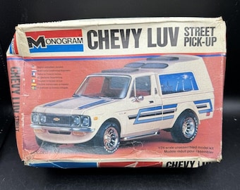 Puede incluir: Una caja de kit de modelo vintage para un camión Chevrolet Luv Street Pick-Up a escala 1/24. La caja presenta una ilustración colorida del camión con rayas azules y blancas, y el texto "MONOGRAM CHEVY LUV STREET PICK-UP" está impreso en la parte delantera.
