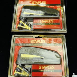 May include: Two packages of black and gold staplers with 1250 standard staples each. The staplers are in clear plastic packaging with red and white branding that says "STAPLES".