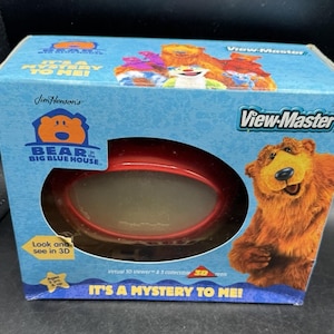Puede incluir: Una caja de View-Master con los personajes de Bear en la Casa Azul Grande. La caja es azul con una ventana de visualización roja y el texto "IT'S A MYSTERY TO ME!". Incluye un visor 3D y carretes coleccionables.