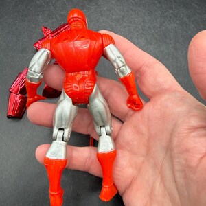 Puede incluir: Figura de acci&oacute;n roja y plateada de un superh&eacute;roe, vista desde atr&aacute;s. La figura tiene un casco, torso y piernas rojos, con brazos y parte inferior de las piernas plateados. La figura es articulada y tiene un accesorio rojo met&aacute;lico.