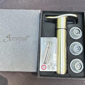 May include: A gold Screwpull wine opener set in a black box with a grey lid. The set includes the opener, three grey stoppers, and a small card. The Screwpull logo is visible on the box, opener, and card.