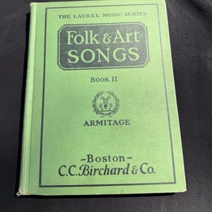 May include: A vintage green book titled "Folk & Art Songs, Book II" from The Laurel Music Series. The cover features the text in a dark green font, with the publisher's name, C.C. Birchard & Co., and the city of Boston at the bottom.