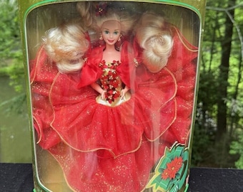 May include: A Barbie doll in a red and gold holiday dress with a poinsettia design. The doll is in a clear plastic box with a gold and green border. The box says "Happy Holidays" and "Special Edition".