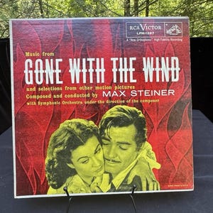 May include: Vintage vinyl record album cover for "Gone With The Wind" featuring a couple embracing. The album cover is red and yellow with the title in large white letters. The RCA Victor logo is in the upper right corner.