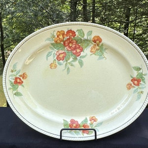 Puede incluir: Un plato de servir ovalado vintage con fondo crema y un diseño floral con flores rojas y naranjas con hojas verdes.
