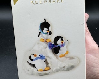 May include: Hallmark Keepsake Christmas ornament featuring three penguins on a snowy hill. The penguins are black and white with colorful scarves. The box reads "Slippin' and Slidin' Special Edition" and "2008 Limited Quantity."