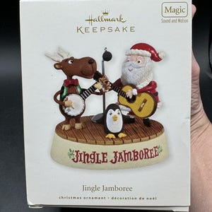 May include: Hallmark Keepsake Christmas ornament featuring a reindeer playing a banjo, Santa Claus playing a guitar, and a penguin. The ornament is titled "Jingle Jamboree" and has a sound and motion feature.