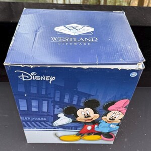 May include: A blue Westland Giftware box featuring Disney's Mickey Mouse and Minnie Mouse. The box has a cityscape background and the Disney logo. The box is a square shape and is made of cardboard.
