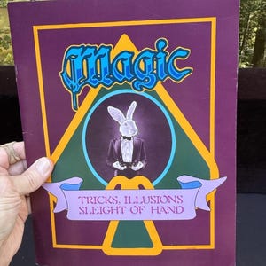 Puede incluir: Un folleto rectangular de color morado titulado Magic en letras azules, con una ilustración central de un conejo blanco con esmoquin y pajarita negros. Debajo del conejo, una pancarta de color morado claro muestra el texto Tricks, Illusions Sleight of Hand.