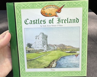 Op de afbeelding: Een groen boek met een groene rand en een afbeelding van een kasteel op de omslag. De titel van het boek is "Castles of Ireland" door de Ierse kunstenares Róisín O'Shea.