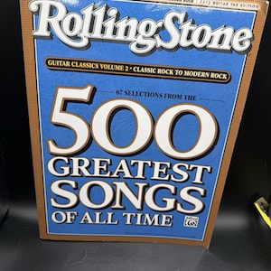 Op de afbeelding: Een Rolling Stone Guitar Classics Volume 2 muziekboek met de tekst 500 Greatest Songs of All Time. De kaft is blauw met bruine randen en witte letters, wat aangeeft dat het een editie is met eenvoudige gitaartabulatuur.