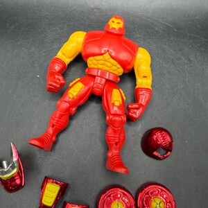 May include: A red and yellow Iron Man action figure with detachable parts, including a helmet and leg armor. The figure is posed with arms outstretched and legs apart, showcasing its detailed design and vibrant colors.