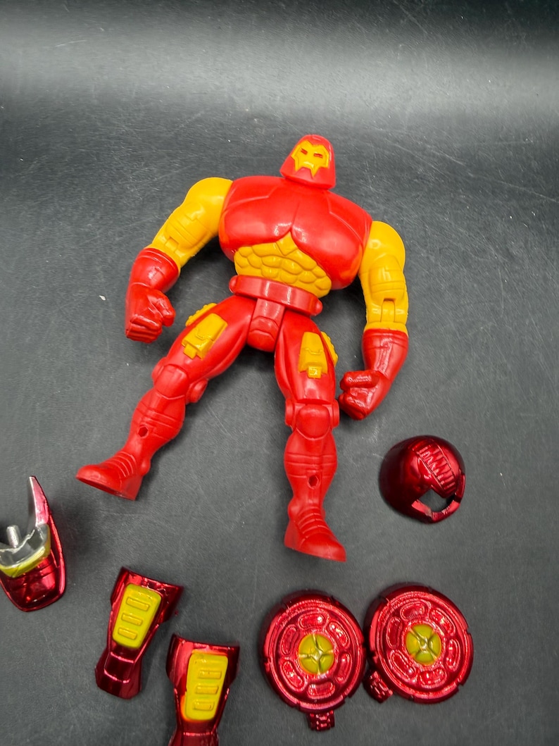 May include: A red and yellow Iron Man action figure with detachable parts, including a helmet and leg armor. The figure is posed with arms outstretched and legs apart, showcasing its detailed design and vibrant colors.