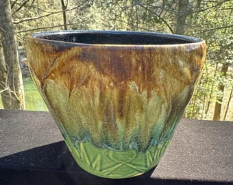 May include: A large, brown and green ceramic planter with a textured, leafy design. The planter has a wide, rounded base and a slightly flared rim.