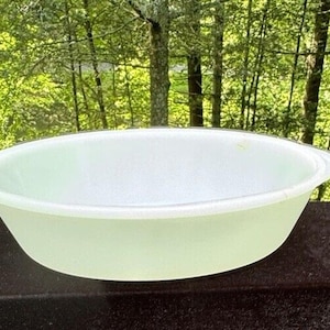 May include: A white oval baking dish with a slightly rippled edge. The dish is sitting on a black surface.
