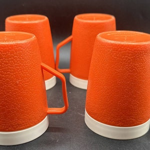 May include: Set of four orange ceramic mugs with white rims. The mugs have a textured surface and are perfect for everyday use.