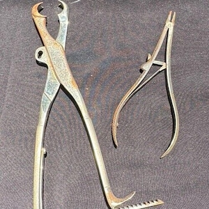 May include: Two antique surgical clamps, one with a serrated edge and the other with a curved tip. Both clamps are made of metal and have a rusty patina.