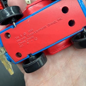 May include: A red and blue toy car with black wheels. The underside of the car features the text "TM & &copy; 1996 Marvel Entertainment Group, Inc. China Chine MT A - 23".