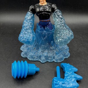 May include: A superhero action figure with a black top, blue pants, and water-like arms and base. Includes two blue accessories. The figure has blonde hair and a determined expression.