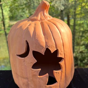 Op de afbeelding: Een keramische pompoen in een warme oranje kleur, met een uitgesneden ster- en halve maan ontwerp. De pompoen heeft een steel en wordt waarschijnlijk gebruikt als Halloween decoratie. De afmetingen zijn ongeveer 20 cm hoog.