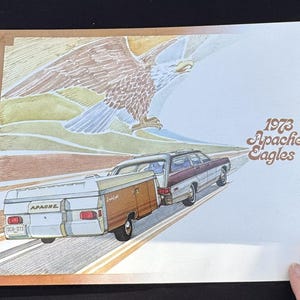 May include: A vintage illustration of a 1973 Apache Eagles station wagon towing a camper. The car is brown and white with a wood-paneled side. The camper is white with a brown roof and the text "Apache" on the side. The illustration is set against a background of a stylized eagle soaring through the sky.