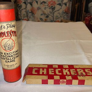 May include: Two vintage game boxes. A red and white tube-shaped box with the text "Let's Play Fiddlestix An Exciting Fascinating Tantalizing Game Plaza Mfg. Co. New York, N.Y.". A brown and red box with the text "Checkers" in white.