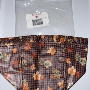 May include: A brown and black gingham fabric liner with a maple leaf print. The liner is for a Longaberger basket. The label reads "LINER-MAPLE LEAF - DINNWR 8U".
