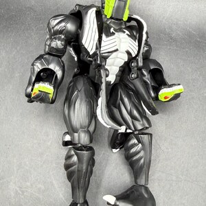 May include: A black and white action figure with a green and red head. The figure has a muscular build with detailed textures and accents. The figure's hands and feet have green and white details.