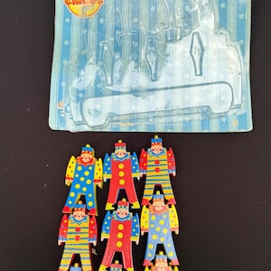 Puede incluir: Un conjunto de nueve payasos de madera apilables en varios colores, incluyendo rojo, amarillo y azul. Los payasos tienen diferentes patrones y diseños. El embalaje dice "Stacking Clowns" y "9 Wooden Clowns Stack, Rock and Balance."