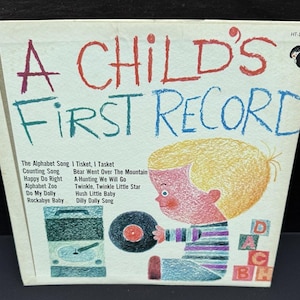 May include: A Child's First Record album cover. The cover features a colorful illustration of a child holding a record. The text includes the album title and a list of songs. The color palette includes red, blue, and yellow.