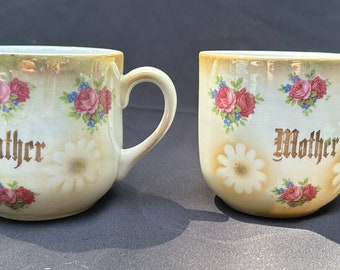 Peut inclure: Deux tasses en céramique blanche avec des motifs floraux et des lettres dorées. Une tasse dit "Père" et l'autre dit "Mère".