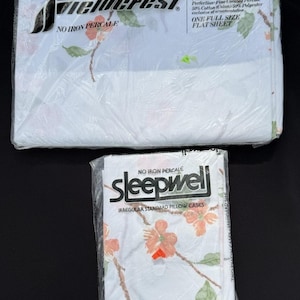 以下が含まれることがあります： FieldcrestのフルサイズフラットシーツとSleepwellの不揃いな標準枕カバーのセット。どちらも透明なプラスチックで包装されており、白い生地にオレンジ色の花と緑の葉のフローラルパターンがプリントされています。