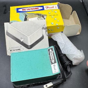 May include: A vintage Metaframe Hush I aquarium filter, with a teal green housing and black cord. The original yellow box features a fish illustration and the text "Hush I". Also included is a gray, rectangular filter component.