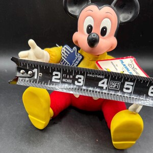 May include: A vintage Mickey Mouse plush doll, featuring a yellow shirt, red pants, and yellow shoes. The doll's face is pink with black eyes and a black nose. The doll is approximately 5 inches long.