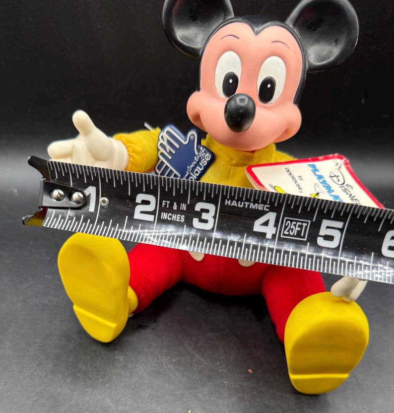 May include: A vintage Mickey Mouse plush doll, featuring a yellow shirt, red pants, and yellow shoes. The doll's face is pink with black eyes and a black nose. The doll is approximately 5 inches long.