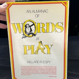 May include: A yellow and red book cover with the title "An Almanac of Words at Play" by Willard R. Espy. The cover features a cartoon illustration of a man in a top hat and a woman riding a man on a horse.