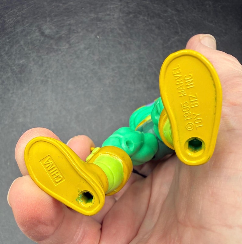 Op de afbeelding: Een vintage actiefiguur, voornamelijk groen en geel. De gele voeten van de figuur dragen de tekst "CHINA" en "&copy;1995 MARVEL TOY BIZ INC.". Het figuur wordt in een hand gehouden.